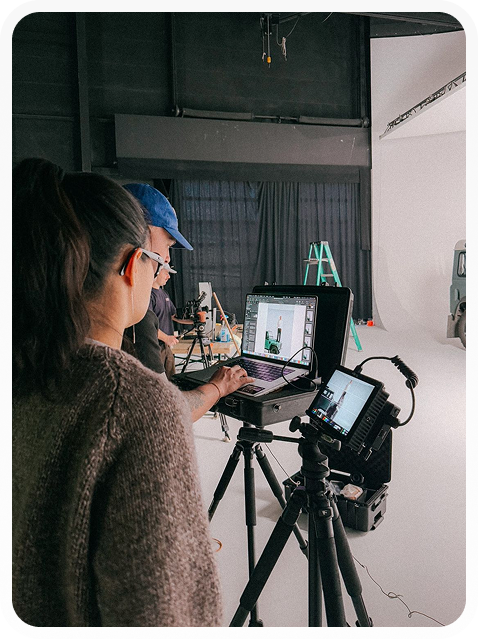 Two people working in a photo studio with camera equipment and a laptop showing product images.